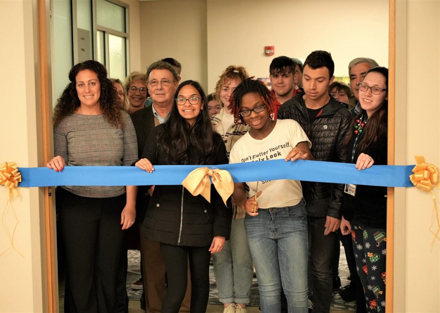 A group of people cutting a ribbon in front of a door.