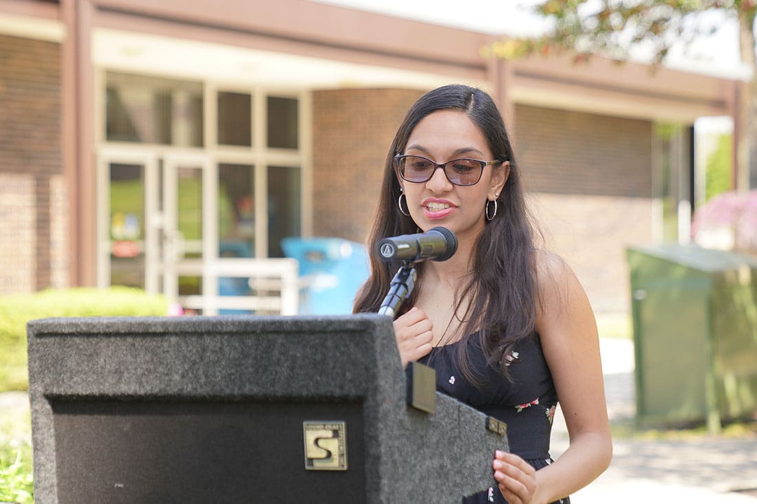 A woman speaking at a podium in front of a building.