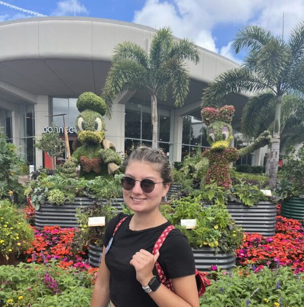 A woman in sunglasses standing in front of a flower garden.