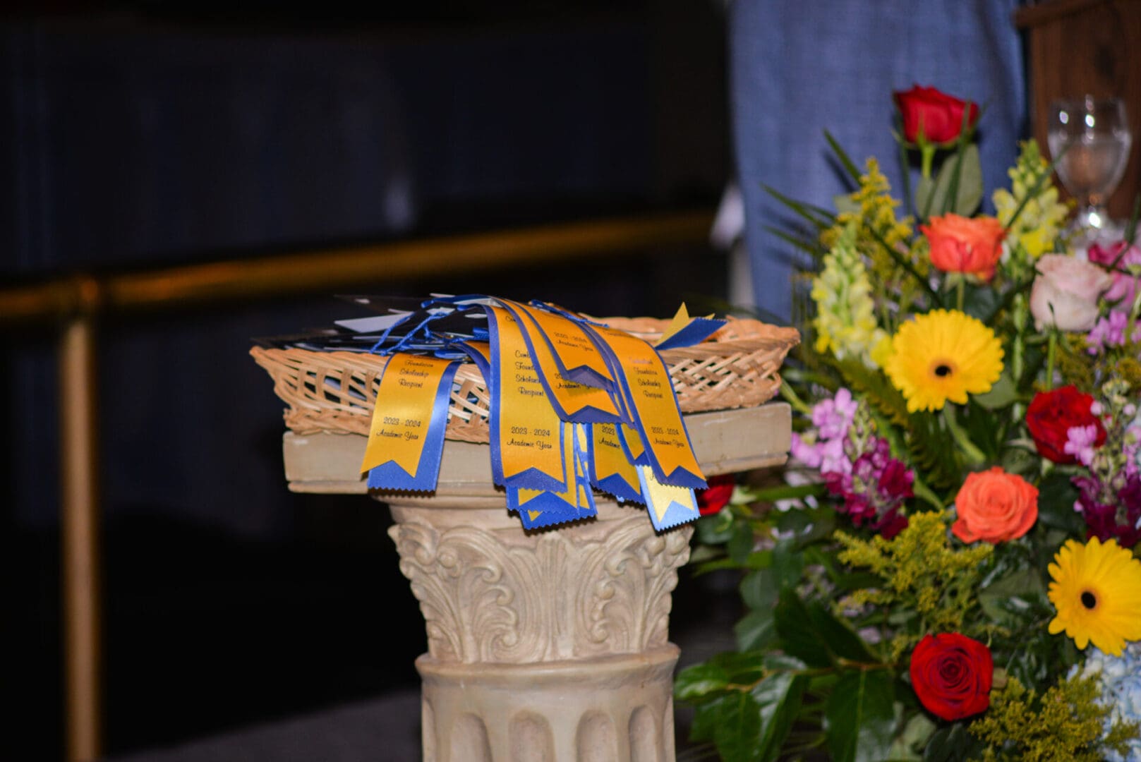 A basket with award ribbons on a pedestal surrounded by colorful flowers.