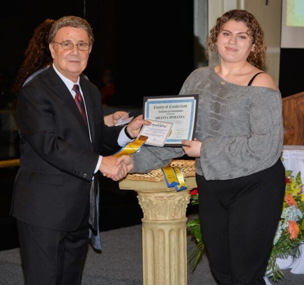 A man and a woman shaking hands at an award ceremony, with the woman receiving a certificate.