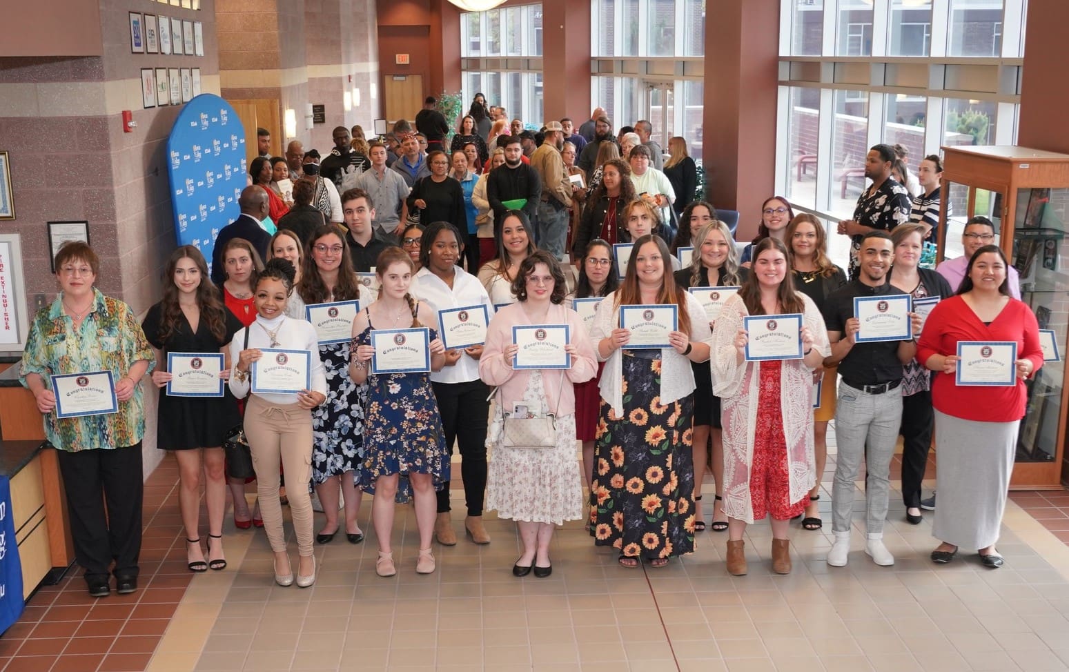 A group of diverse people holding certificates in a lobby during an awards ceremony.