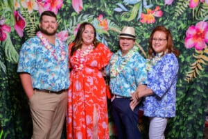 Four people in tropical attire standing in front of a vibrant floral backdrop.