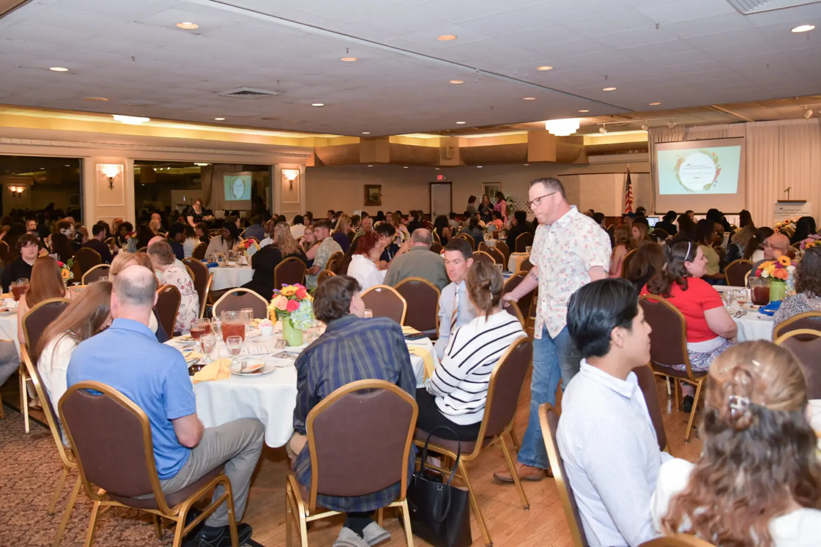 Guests socializing at a large indoor banquet event with round tables.