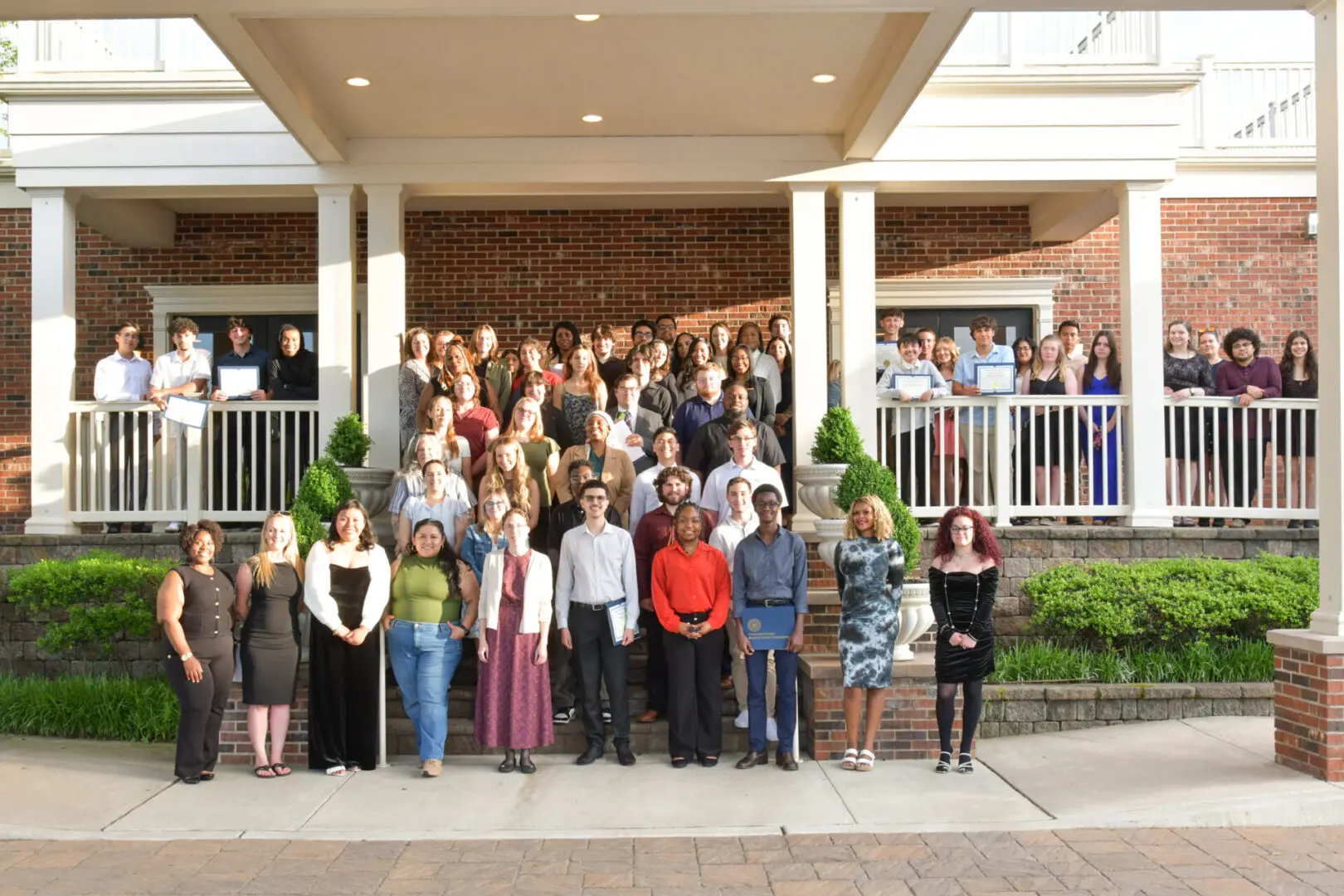 Large group photo taken on a porch with people dressed in formal and semi-formal attire.
