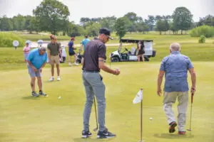 People playing golf on a sunny day with golf carts in the background.