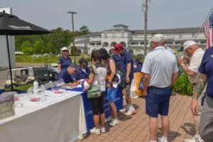 People gathered at an outdoor event registration table on a sunny day.